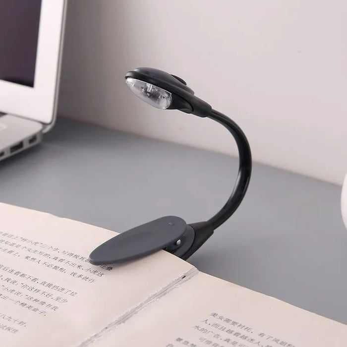 Black flexible book light on an open book with a laptop in the background