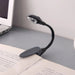 Black flexible book light on an open book with a laptop in the background