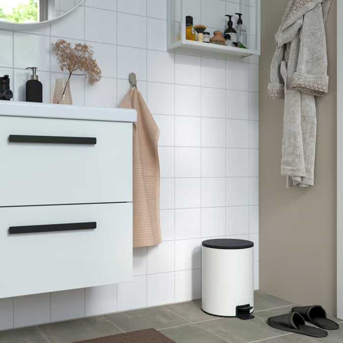 Modern white pedal bin used in a tiled bathroom setting next to a white vanity cabinet.