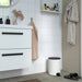 Modern white pedal bin used in a tiled bathroom setting next to a white vanity cabinet.