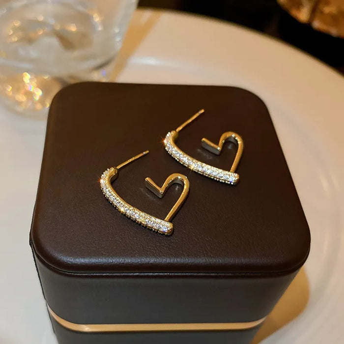 Brown jewelry box with gold and diamond-encrusted earrings on a white surface.