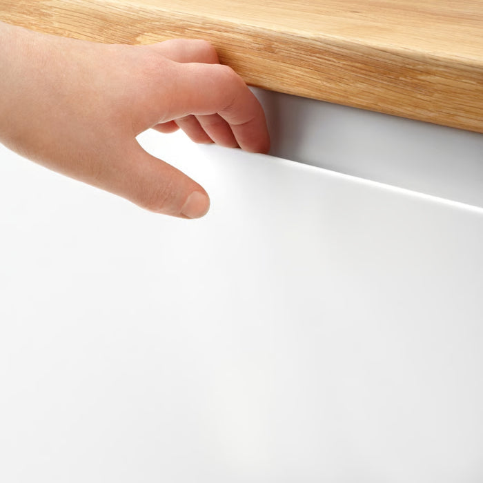 Hand reaching under a white cabinet door with a wooden top.
