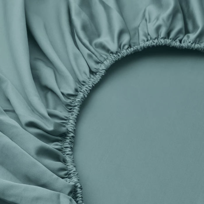 Teal fitted sheet on a bed with a close-up of the fabric and stitching.