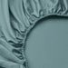 Teal fitted sheet on a bed with a close-up of the fabric and stitching.