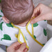 IKEA KLADDIG bib being fastened on a child—white with green dots and yellow trim, secured at the neck for snug fit – 70607142.