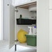 Open white cabinet with cleaning supplies including a yellow plate, green bin, and bottles.