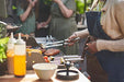 Person grilling food outdoors with a crowd in the background