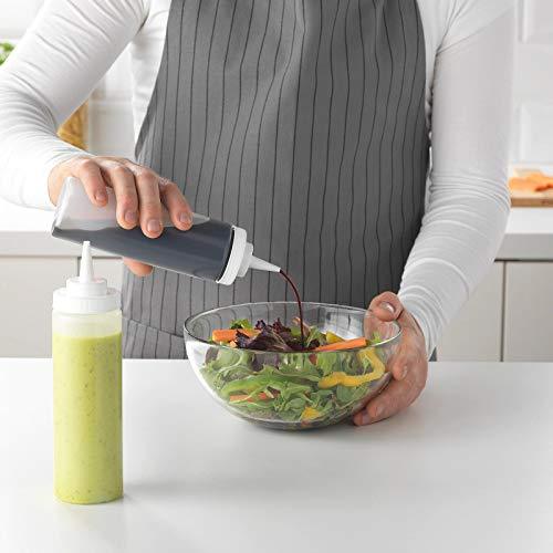 Person pouring dressing from a squeeze bottle onto a salad in a kitchen setting.