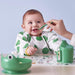 IKEA KLADDIG bib worn by a child—white base with green polka dots, yellow trim, and long sleeves; child is being spoon-fed at a table – 70607142.