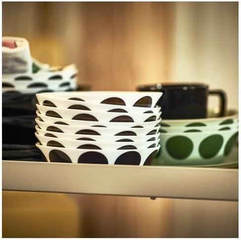 Shelf display featuring a stack of white IKEA OFTAST bowls with bold black semi-circle patterns around the outer rim—accompanied by a black handled mug and a green plate with dotted black circle motifs.- 10608267