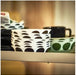 Shelf display featuring a stack of white IKEA OFTAST bowls with bold black semi-circle patterns around the outer rim—accompanied by a black handled mug and a green plate with dotted black circle motifs.- 10608267