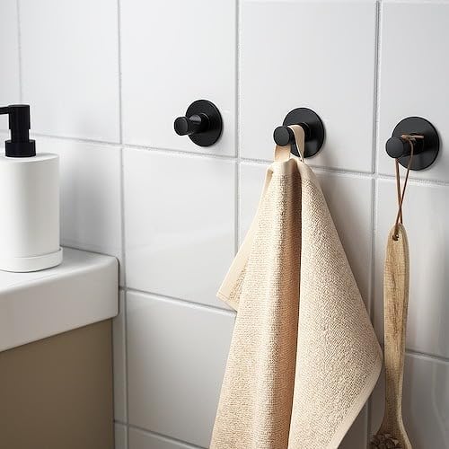 Black wall hooks with beige towels on a tiled bathroom wall.