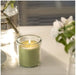 Lit green candle in glass placed beside vase with leaves and white flowers – 50582053