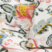 Close-up of floral cotton fabric with pink, yellow, blue, and green flowers and leaves on white background, showing snap button closure detail.

