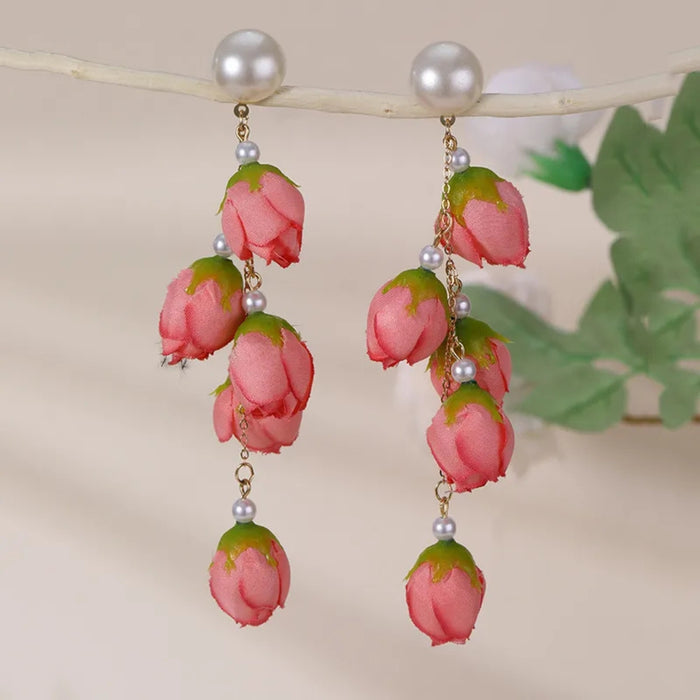 Digital Shoppy red bud earrings – close-up of red rosebud earrings hanging from branch with soft-focus green leaves

