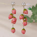 Digital Shoppy red bud earrings – close-up of red rosebud earrings hanging from branch with soft-focus green leaves

