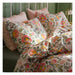 Floral bedding set on a bed with pink pillows against a green wall.