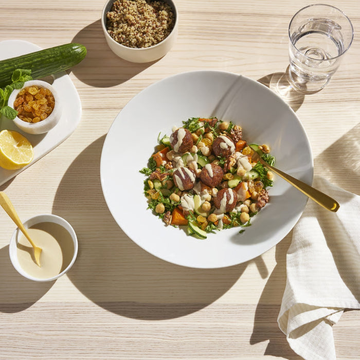 Plated salad with meat and vegetables on a wooden table with lemon, zucchini, and water.