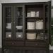 Dark wooden cabinet with open doors displaying various items including plates, baskets, and folded clothes.