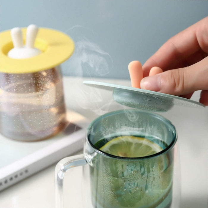 Glass mug with lemon slices and rising steam, covered by bunny ear silicone lid – hand lifting lid to reveal hot drink – 1598447679156 13987144