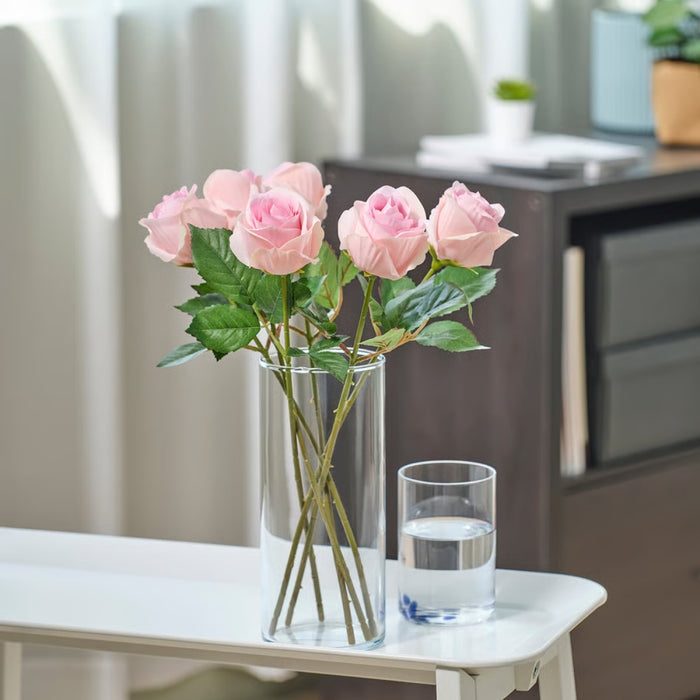 Clear vase with pink roses on a white surface with a blurred background