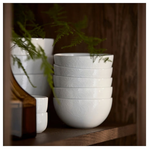Stack of white ceramic bowls on a wooden shelf with plants in the background