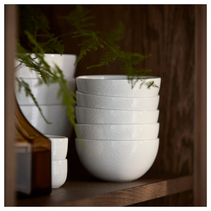 Stack of white ceramic bowls on a wooden shelf with plants in the background