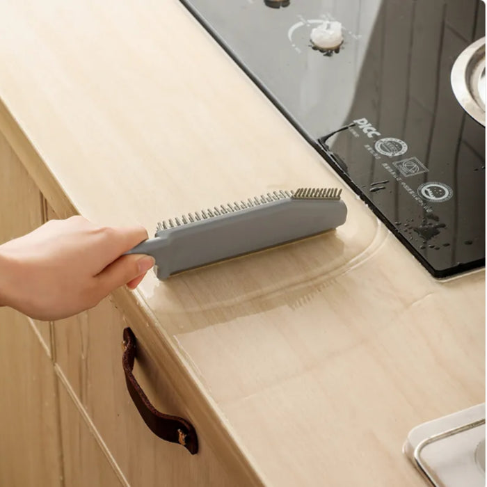 Person using a gray brush to clean a kitchen counter next to a stove.