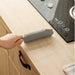 Person using a gray brush to clean a kitchen counter next to a stove.