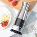 Stainless steel manual food chopper placed on a book with text, beside a white plate of chopped garlic and peppers; wooden board with whole red peppers in background – 1600000766929 13074717.