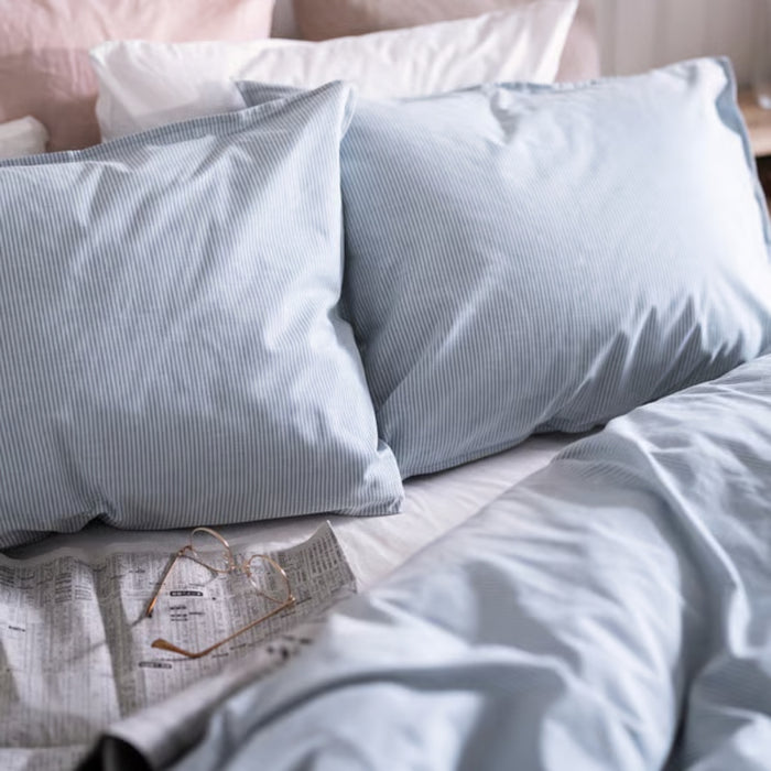 BERGPALM pillowcase, blue/striped, 50x80 cm. Shown on bed with matching duvet cover, white and pink pillows, newspaper and glasses – cosy, lived-in bedroom vibe – 50577117.