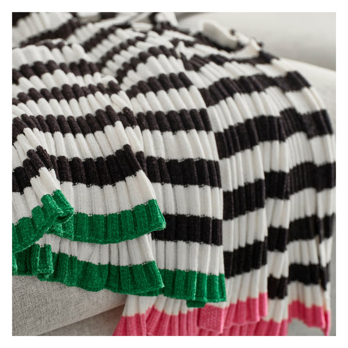 Black, white, and green striped blanket with pink trim on a couch.