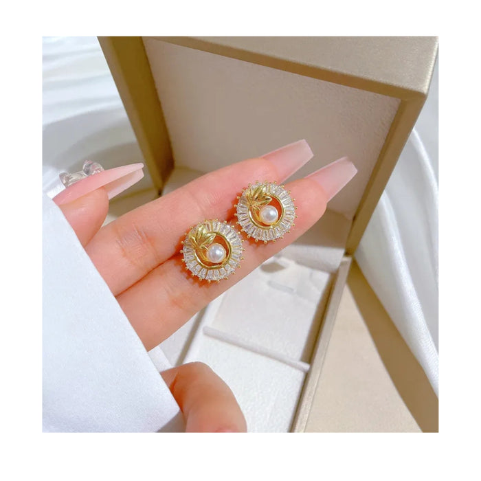 Gold and pearl earrings held by a hand with a white background