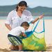 Woman and child with a green mesh beach bag on a sandy beach.