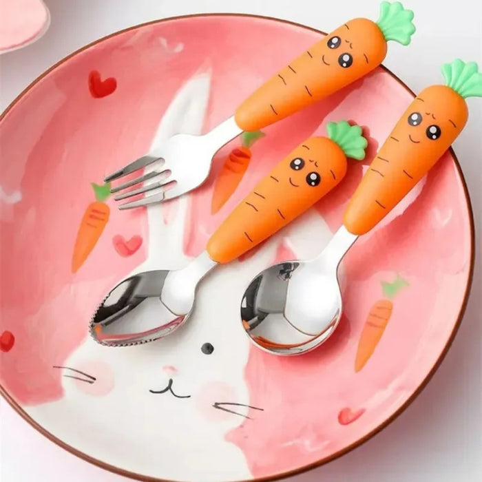 Children’s carrot-themed tableware set displayed on a pink bunny-face plate with carrot illustrations—includes a stainless steel fork and two spoons with bright orange handles shaped like carrots, each topped with a smiling face and green leafy detail; playful, kid-friendly design enhances mealtime enjoyment – 1600002332714 12850097.