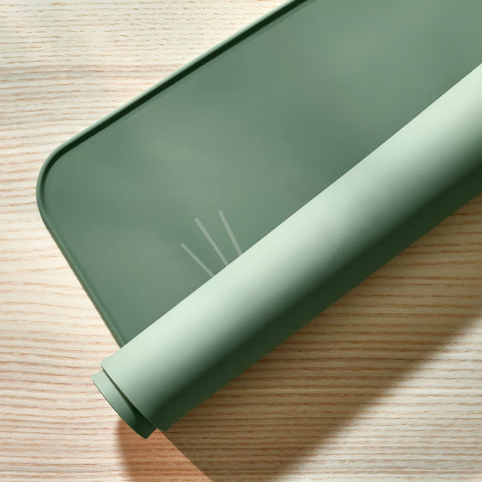 Rolled-up green silicone mat with smooth texture and white printed lines, placed on a wooden surface.