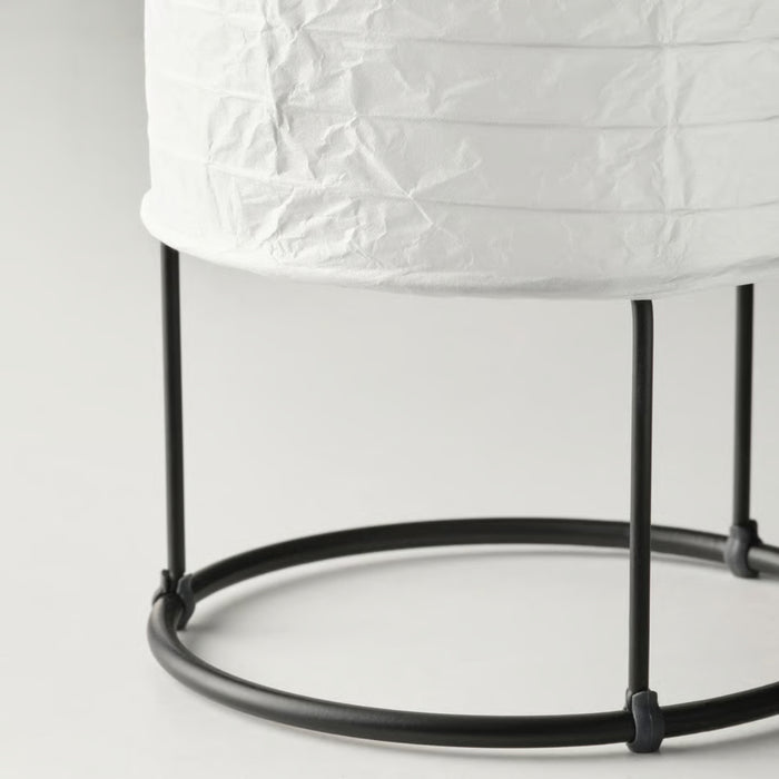 Close-up of IKEA STRANDAD table lamp with white crinkled paper shade and black metal frame; cylindrical design with three vertical rods and round base – 20594849