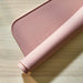 Rolled-up pink silicone mat with smooth texture and subtle white line design, placed on a wooden surface.