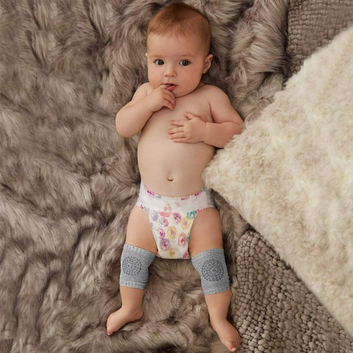 Baby anti-slip knee pads – baby lying on plush rug wearing floral diaper and grey protective pads