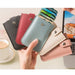 Hand holding a light blue cardholder with cards, surrounded by other cardholders in different colors on a desk.