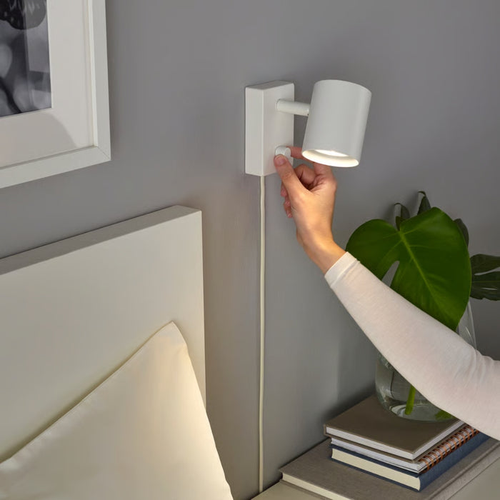 Hand adjusting a wall-mounted light fixture on a gray wall.