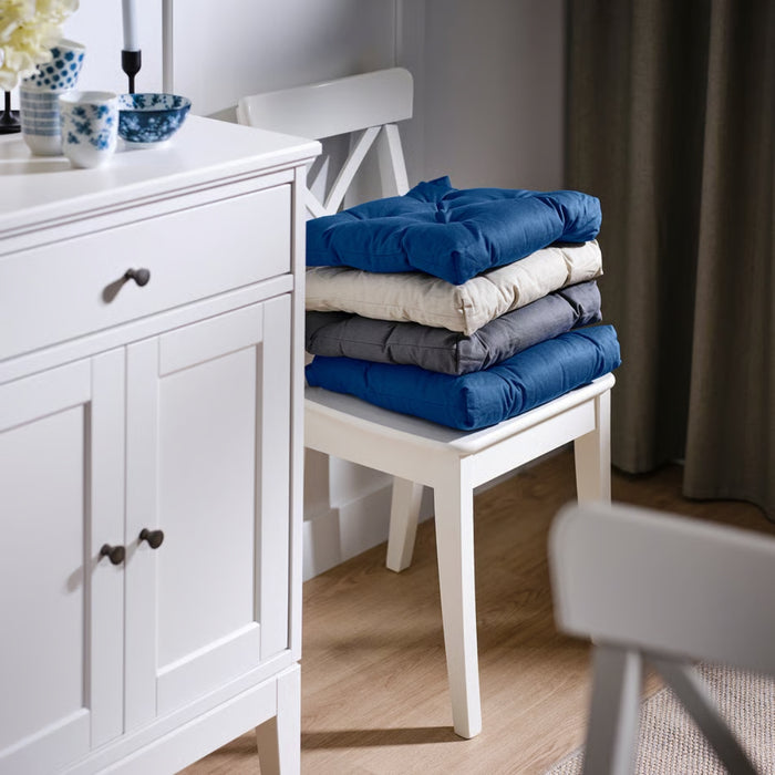 Stack of folded blue, gray, and white clothes on a white chair next to a white cabinet.