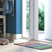 Colorful doormat on a wooden floor with a blue wall and sliding glass door in the background.