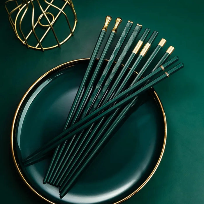 Green chopsticks with gold tips on a green plate against a matching background