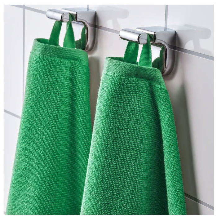 Two green towels hanging on a silver towel rack against a tiled wall.
