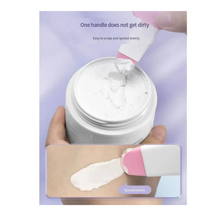 White jar with pink scoop being used to spread a white substance on a hand against a light purple background.