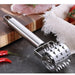 Metal meat tenderizer on a dark surface with red peppers and a wooden cutting board in the background.