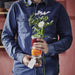 Person holding a stack of glass jars with flowers and a tag, wearing a blue shirt.