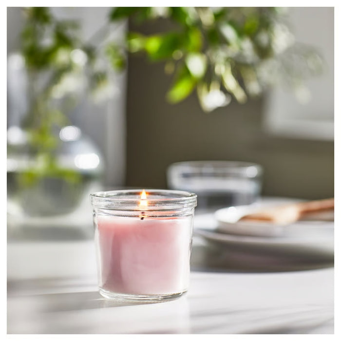 Lit IKEA LUGNARE scented candle in pink glass with jasmine aroma, placed on white surface; soft natural light and serene home decor in background – 20-hour burn time - 00502110