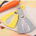 Two kitchen graters, one yellow and one gray, on a surface with vegetables.